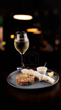 Téléchargez les photos : Tartare de saumon cru avec sauce grillée et citron associé au vin blanc dans un restaurant - en image libre de droit