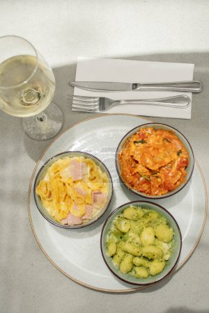Téléchargez les photos : Assortiment avec différents plats de pâtes et verre de vin blanc gnocchi pesto tagliatelle et ravioli vue de dessus - en image libre de droit