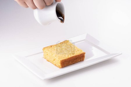 assiette blanche avec la main de gâteau de carotte sur le point de verser des gouttes de garniture de chocolat gros plan