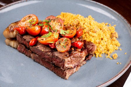 Foto de Dos trozos de solomillo cocido con grasa, ensalada de tomate cherry y farofa en una cena de asador con perejil - Imagen libre de derechos