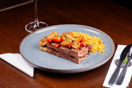 Foto de Plato de dos trozos de solomillo cocido con grasa, ensalada de tomate cherry y farofa en una cena en el asador - Imagen libre de derechos