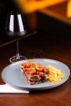 Foto de Filete de solomillo perfectamente cocido con grasa, ensalada de tomate cherry y farofa en una cena en el asador, fondo borroso y copa de vino tinto - Imagen libre de derechos