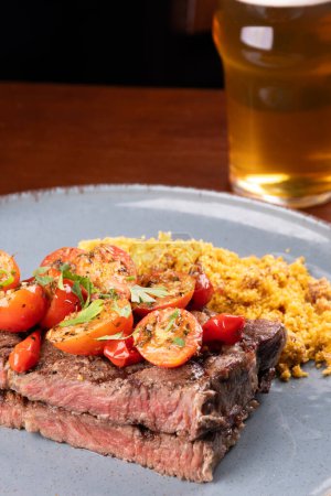 Foto de Filete de solomillo perfecto con ensalada de tomate cherry y farofa en una cena en el asador con un vaso de cerveza - Imagen libre de derechos