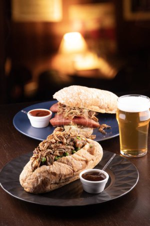 Rindereintopf-Sandwich mit knusprigen Zwiebeln und Gemüse und Barbecue-Sauce auf dunklem Hintergrund und Wurst-Sandwich mit
