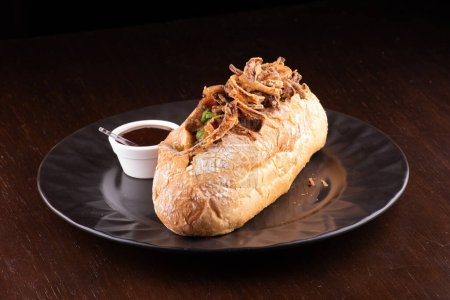 Rindereintopf-Sandwich mit knusprigen Zwiebeln und Gemüse und Barbecue-Sauce auf dunklem Hintergrund