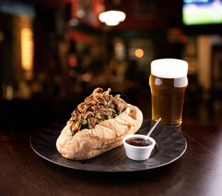beef stew sandwich with crispy onion and vegetables and barbecue sauce with half pint of beer and blurred pub background