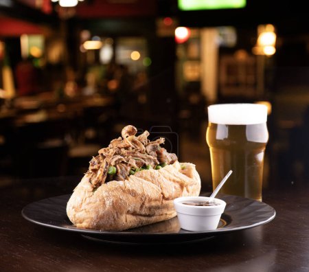 beef stew sandwich with crispy onions and vegetables and barbecue sauce with half pint of beer and blurred pub background