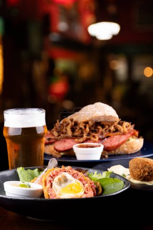 bar junk food with scotch egg, fish cake and sausage sandwich with crispy onion with artesnala beer and blurred bar