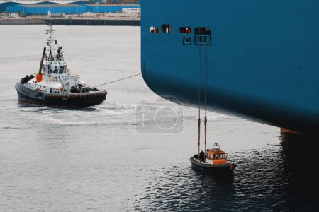 Mooring operation. Docking of the cargo vessel in the port. Tug boat and linesmen in the boat taking the mooring line from the big ship.