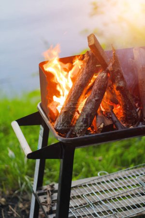 Photo for Brazier is full of dried wood on the fire. Barbecue outdoors in the forest on a lake. Preparations for roasting the meet. Picnick with family loved ones friends. - Royalty Free Image