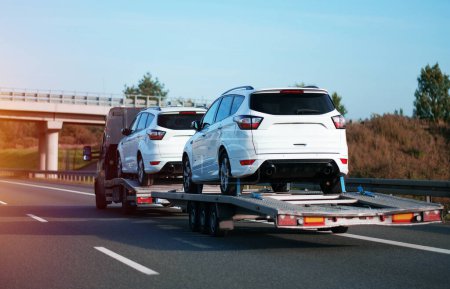 Foto de Transporte seguro de los nuevos coches SUV blancos vistos en la carretera con la ayuda de un transportador de carga pesada - Imagen libre de derechos