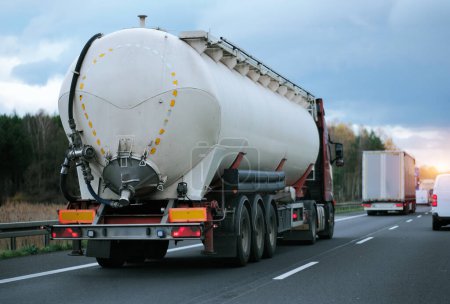 Petrol truck on highway hauling fossil oil refinery products. Fuel delivery transportation. Aviation fuel transportation. Compressed gas carrier truck rear view on a highway. Dairy products carrier