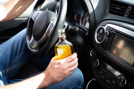 Fahrer fährt Auto mit einer Flasche Alkohol in der Hand aus nächster Nähe.