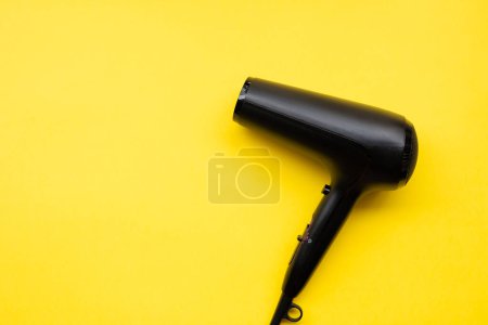 Black hair dryer on blue and yellow paper background