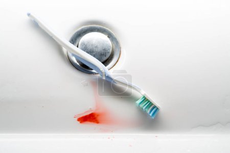 Zahnbürste in einem weißen Waschbecken mit Blut. Problem mit dem Zahnfleisch.
