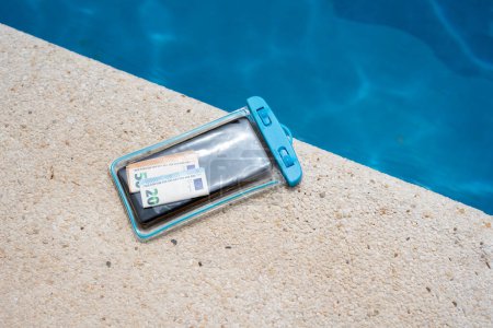 Wasserdichte Tasche mit Geld und Smartphone auf dem Hintergrund des Pools an einem sonnigen Sommertag.