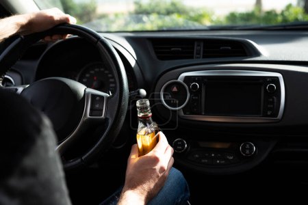 Conductor conduciendo un coche con una botella de alcohol en sus manos de cerca.