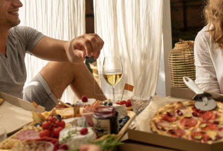 Téléchargez les photos : Fille avec un verre de vin mange une pizza assortie au lit avec des rayons de soleil sur le lit. Photo de haute qualité - en image libre de droit