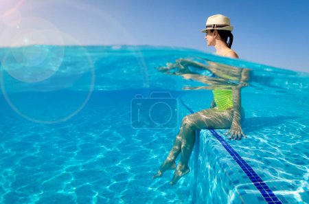 Téléchargez les photos : Belle jeune femme souriante sexy dans la plage de la piscine d'été. Fille se détendre dans la piscine tropicale par temps ensoleillé, éclaboussures d'eau avec les pieds, spa. Fractionnement sous-marin - en image libre de droit