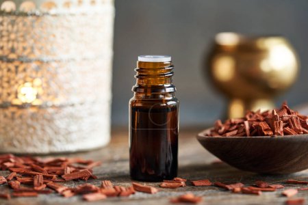 Photo for Dark bottle of essential oil with red sandalwood chips and an aroma lamp - Royalty Free Image