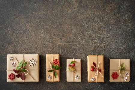 Téléchargez les photos : Cadeau de Noël enveloppé dans du papier recyclé écologique avec des brindilles d'hiver sur fond sombre avec espace de copie - en image libre de droit