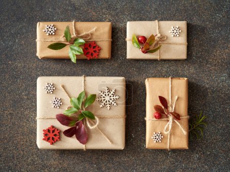 Photo for Christmas present boxes wrapped in ecological recycled paper with fresh wintergreen and wooden decoration on dark background - Royalty Free Image