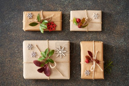 Téléchargez les photos : Quatre cadeaux de Noël enveloppés dans du papier recyclé écologique avec des feuilles et des baies fraîches d'hiver - en image libre de droit