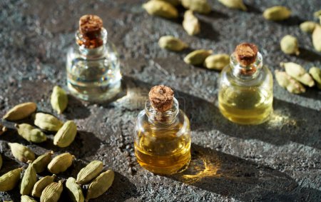 Photo for Bottles of aromatherapy essential oil with cardamom seeds on dark background - Royalty Free Image