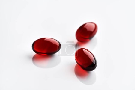 Tres píldoras de aceite de krill rojo o glóbulos sobre fondo blanco