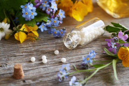Foto de Una botella de vidrio con glóbulos homeopáticos derramados, con hierbas y flores de primavera - Imagen libre de derechos
