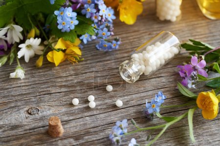 Foto de Pastillas homeopáticas en una botella con coloridas flores de primavera sobre una mesa - Imagen libre de derechos