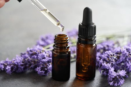 Foto de Dejando caer el aceite esencial de aromaterapia en una botella de vidrio oscuro, con flores de lavanda fresca en el fondo - Imagen libre de derechos