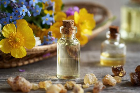 A transparent bottle of aromatherapy essential oil with frankincense resin and colorful spring flowers