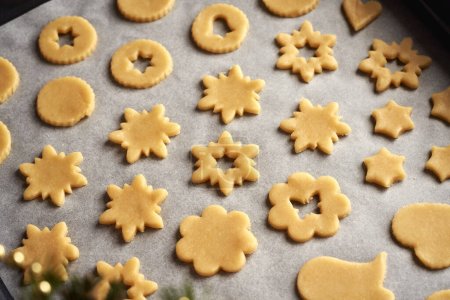 Foto de Estrella y otras formas hechas de masa de pastelería en una hoja de papel de hornear - preparación de galletas de Navidad Linzer - Imagen libre de derechos