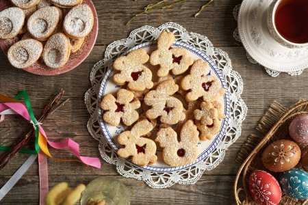Homemade Linzer cookies in the shape of animals on a plate, with Easter eggs decorated with wax, top view