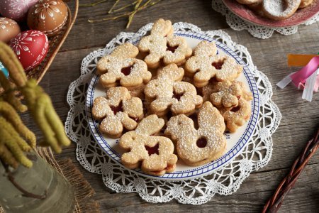 Homemade Linzer cookies in the shape of cute animals, with Easter eggs decorated with wax in the background