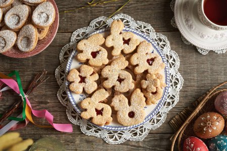 Homemade Linzer cookies in the shape of bunnies and chicken, with Easter eggs in the background