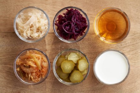 Top view of fermented foods in bowls - kimchi, white and purple sauerkraut, apple cider vinegar, gherkins and kefir