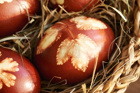Huevos de Pascua marrones teñidos con cáscaras de cebolla con un patrón de hojas en una canasta, de cerca