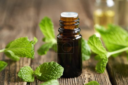 Una botella marrón de aceite esencial de aromaterapia con hojas de menta fresca     