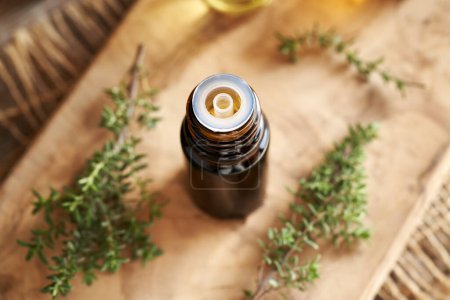 Photo for A dark bottle of aromatherapy essential oil with fresh thyme plant on a wooden table - Royalty Free Image