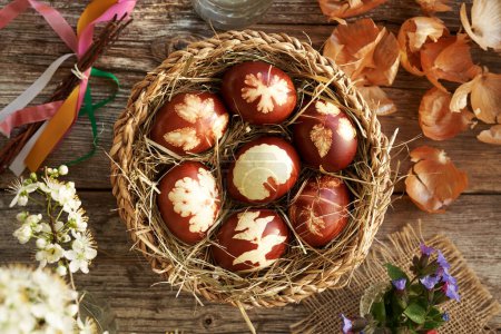 Huevos de Pascua marrones teñidos con cáscaras de cebolla con un patrón de hojas en una canasta de mimbre, vista superior