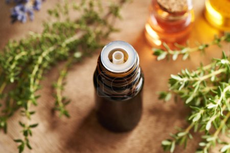 Photo for A brown bottle of aromatherapy essential oil with fresh thyme plant, close up - Royalty Free Image