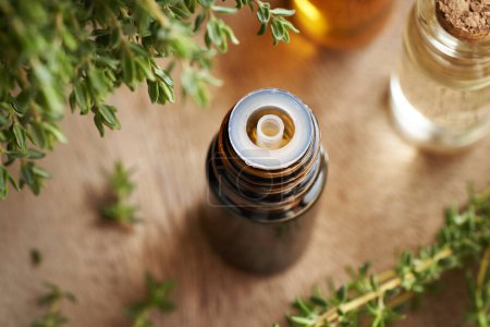 Photo for A dark bottle of aromatherapy essential oil with fresh thyme twigs on a wooden table - Royalty Free Image