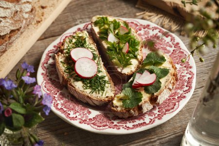 Spring wild edible plants - garlic mustard onion grass and goutweed, on three slices of sourdough bread