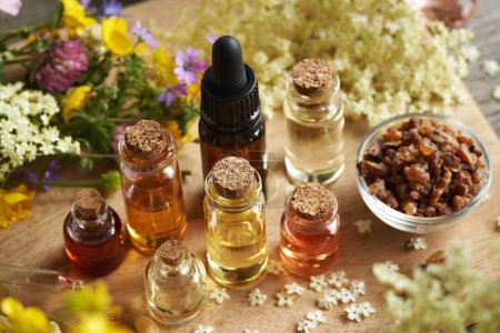 Bottles of aromatherapy essential oil with myrrh, frankincense and colorful spring flowers on a table