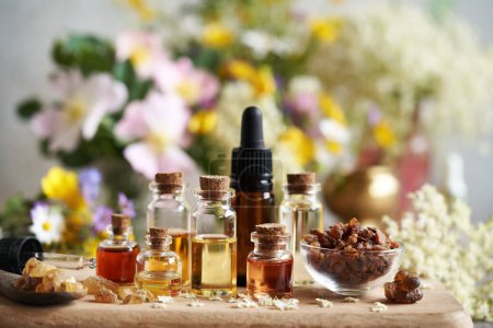 Several bottles of aromatherapy essential oil with myrrh, frankincense and colorful spring flowers on a table