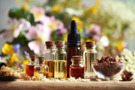 Bottles of aromatherapy essential oil with myrrh, frankincense and spring flowers on a table