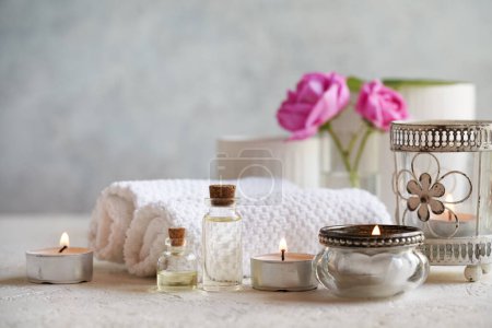 Bottles of aromatherapy essential oil with candles, rose de Mai flowers and spa treatment accessories on bright background