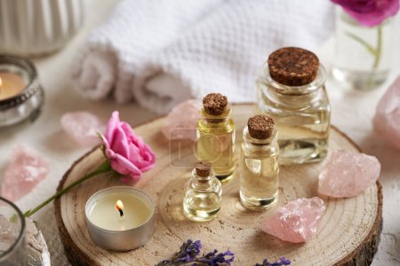 Bottles of aromatherapy essential oil with lavender and rose flowers, rose quartz stones and spa treatment accessories on a table